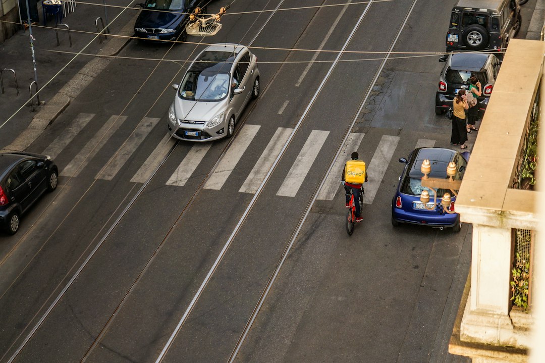 Delivery person on scooter crosses street near cars