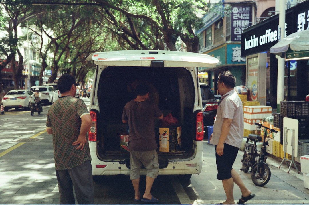 Three men around an open white van on a tree-lined city street