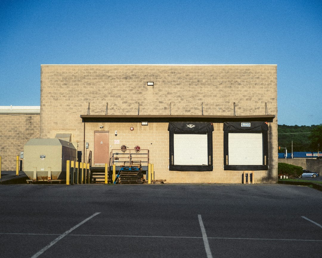 A beige concrete warehouse building with two loading docks and a dumpster